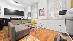 A modern living room with a grey sectional sofa, a glass coffee table, and a patterned rug. - 3BG Historic Flat 1BR sleeps 4 Aircon Balcony (London)