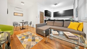 A modern living room with a glass coffee table, a sofa with yellow cushions, and a dining area with a small table and chairs. - 3BG Historic Flat 1BR sleeps 4 Aircon Balcony (London)