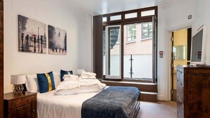 A hotel room with a bed, a nightstand, a dresser, and two paintings on the wall. - 3BG Historic Flat 1BR sleeps 4 Aircon Balcony (London)