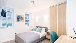 Un dormitorio moderno con cama, mesitas de noche, un escritorio y un armario.