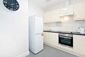 Kitchen features a refrigerator and oven, along with light-colored cabinetry and a black countertop.