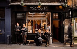 Un café appelé Monmouth Coffee Company, avec une façade noire et de grandes vitrines où sont exposés divers produits.