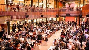 A crowded indoor space with multiple levels of seating areas, railings, and a variety of people engaged in different activities.