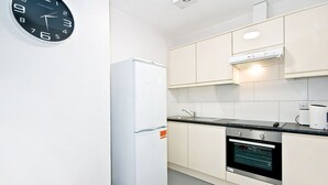 A modern kitchen with a built-in oven, a refrigerator, and a wall-mounted clock.