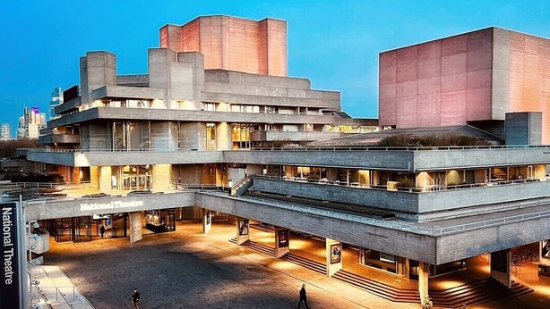 A multi-story building with a flat roof and a large open plaza in front.