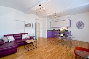 Un salon moderne avec un canapé violet, une table à manger en verre et un coin cuisine doté de meubles violets.