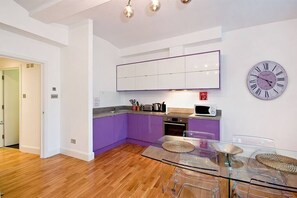 Une cuisine moderne avec des meubles de couleur violette, une table à manger en verre et une horloge murale.