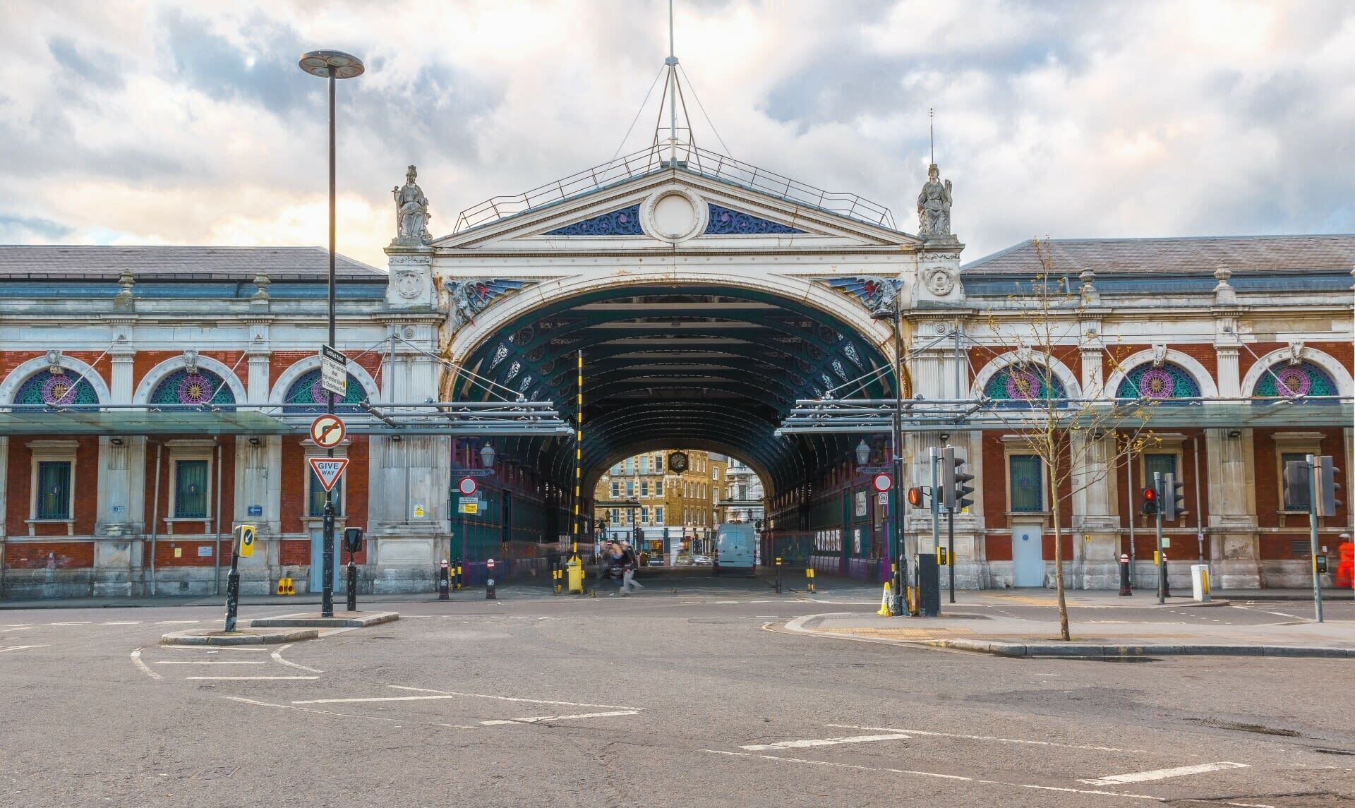 A grand archway with intricate designs and statues on either side, leading to a building with ornate windows and a clock tower.
