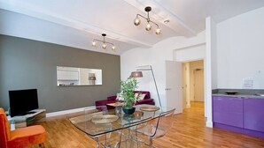 Un salon moderne avec une table à manger en verre, un canapé rouge, un téléviseur et un coin cuisine doté de meubles violets.