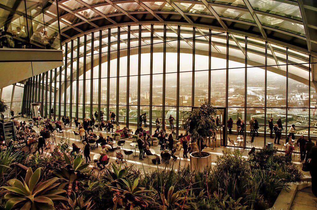 A spacious indoor atrium with a curved glass ceiling, allowing natural light to illuminate the area.