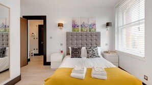 Een hotelkamer met een groot bed, een gestoffeerd hoofdbord, twee nachtkastjes, een spiegel en een raam met luxaflex.