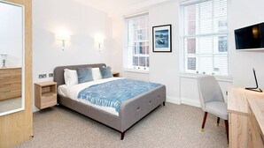 A modern bedroom with a bed, bedside tables, a chair, and a TV. - P1E Double Room Private Shower air con wifi (London)