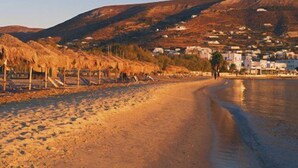 A beach with thatched-roof huts, a calm sea, and a town in the background. - An apartment that sleeps 4 guests  in 1 bedroom (Paros)
