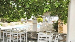 An outdoor patio area with stone flooring, white wooden tables and chairs, and a view of a swimming pool. - An apartment that sleeps 4 guests  in 1 bedroom (Paros)