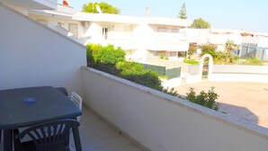 Un balcon avec une table et des chaises, donnant sur un quartier résidentiel avec des maisons et de la verdure.
