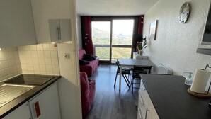 Een moderne keuken met een zwart aanrecht, witte kasten en een rode bank in de woonkamer.
