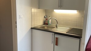 Een kleine keuken met witte kastjes, een roestvrijstalen spoelbak en een ingebouwde kookplaat.