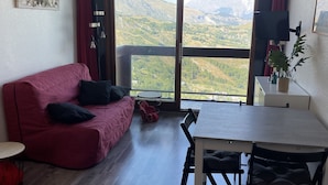Een moderne woonkamer met een rode bank, een eettafel met stoelen en een groot raam met uitzicht op bergen.