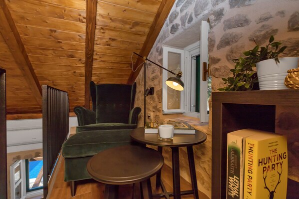 Una habitación acogedora con vigas de madera, un sofá verde, una mesita con una vela y una estantería llena de libros.