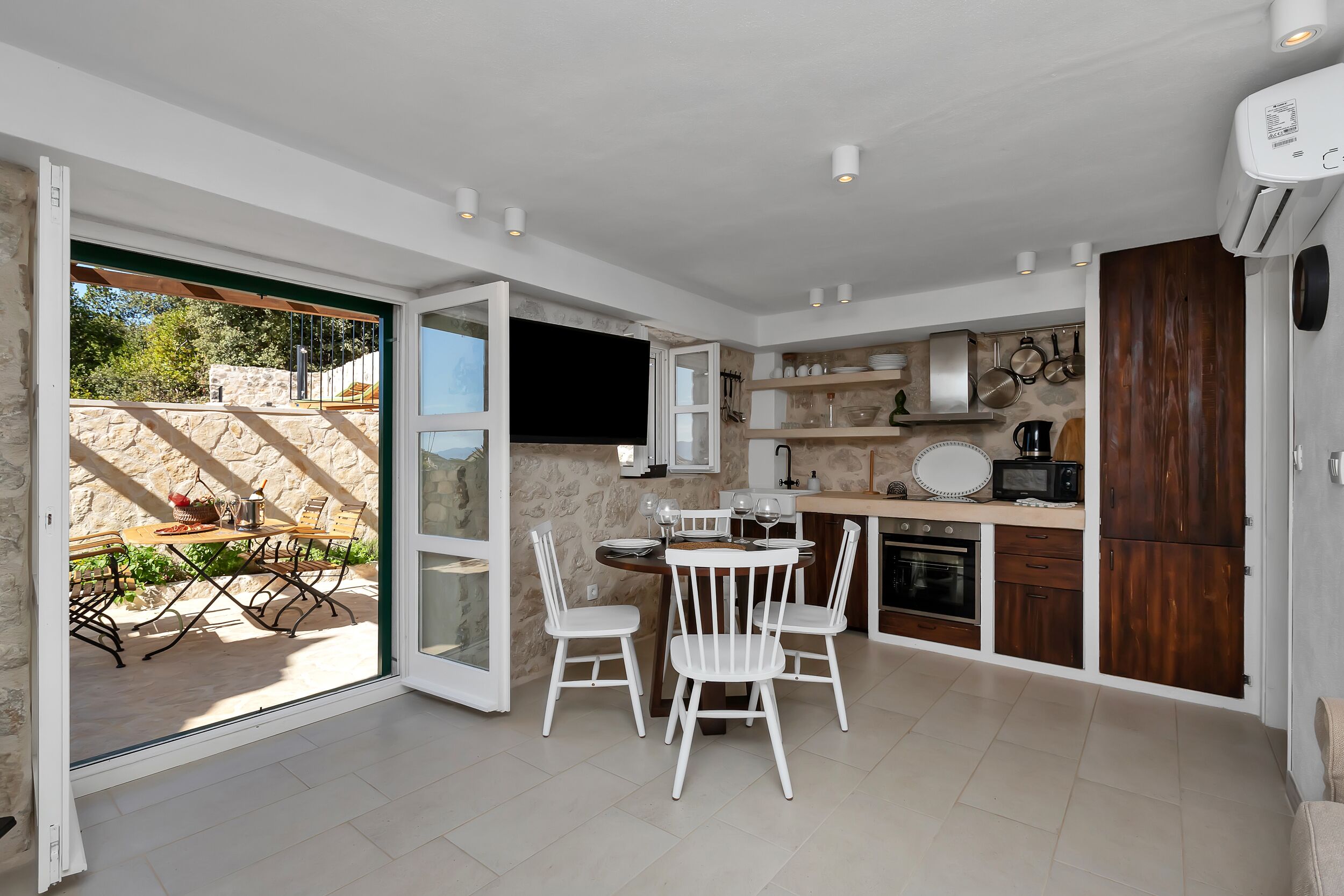 Une cuisine moderne avec des meubles blancs, un coin repas avec des chaises blanches et une vue sur la terrasse extérieure.