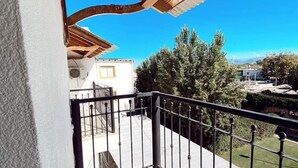 Un balcó amb una pèrgola de fusta, barana metàl·lica i vista a una zona residencial amb arbres i edificis.