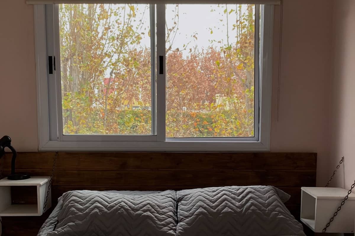 A bedroom with a bed, pillows, a nightstand, a lamp, and an air conditioner.
