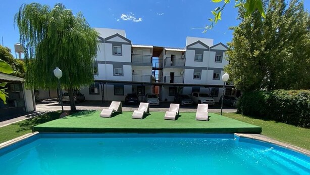 Una piscina amb gandules, un edifici amb balcons i un salze plorant.