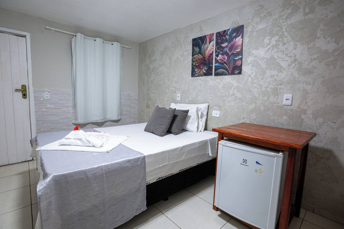 A small, clean room with a bed, a small table, and a refrigerator.