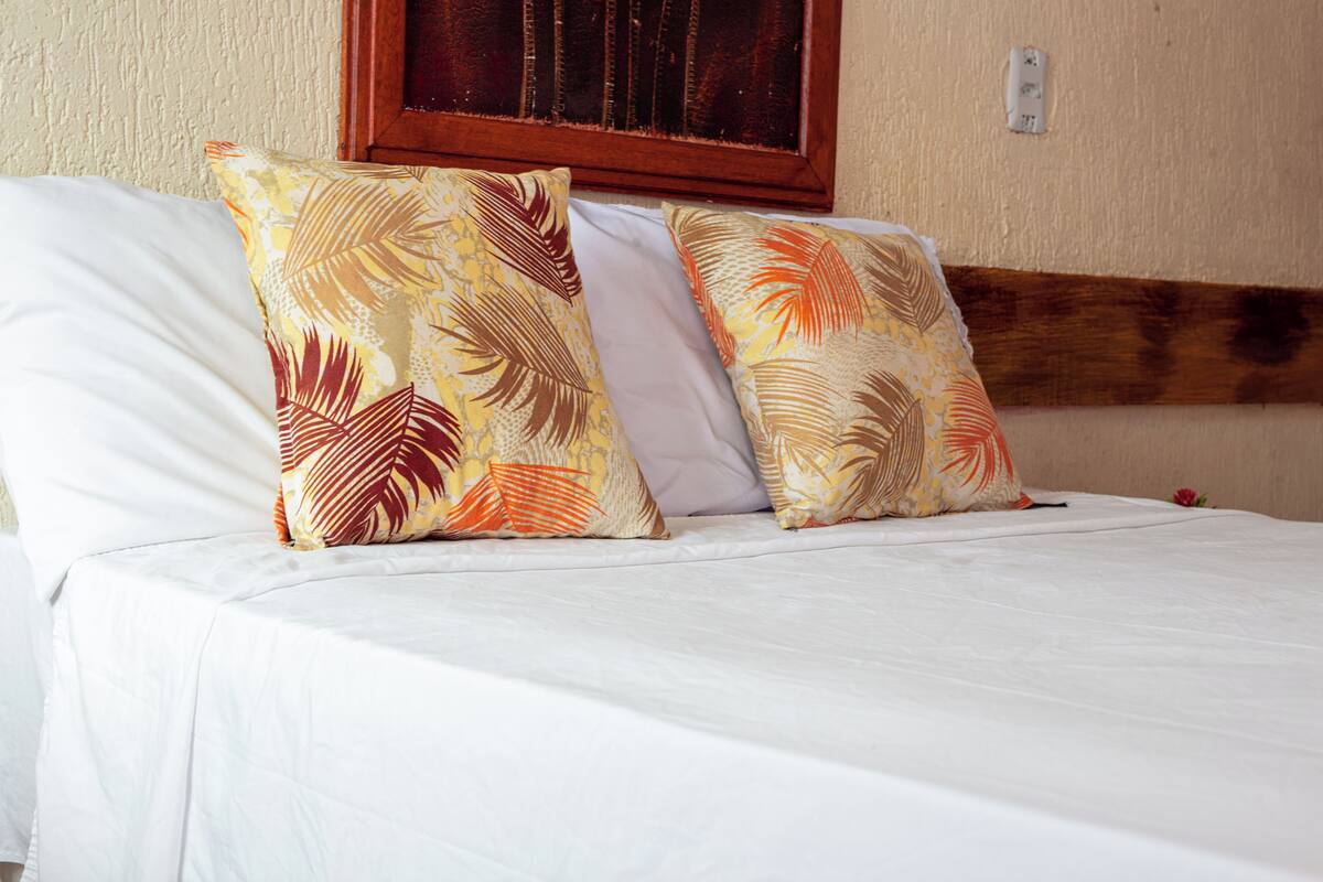 A bed with white bedding and two decorative pillows with a tropical leaf pattern.