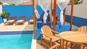 A poolside area with wooden lounge chairs, a table, and a canopy structure. - Rede Andrade Porto Center Hotel (Porto Seguro)