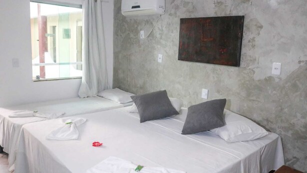 A hotel room with two beds, a window with curtains, an air conditioning unit, and a painting on the wall. - Rede Andrade Porto Center Hotel (Porto Seguro)