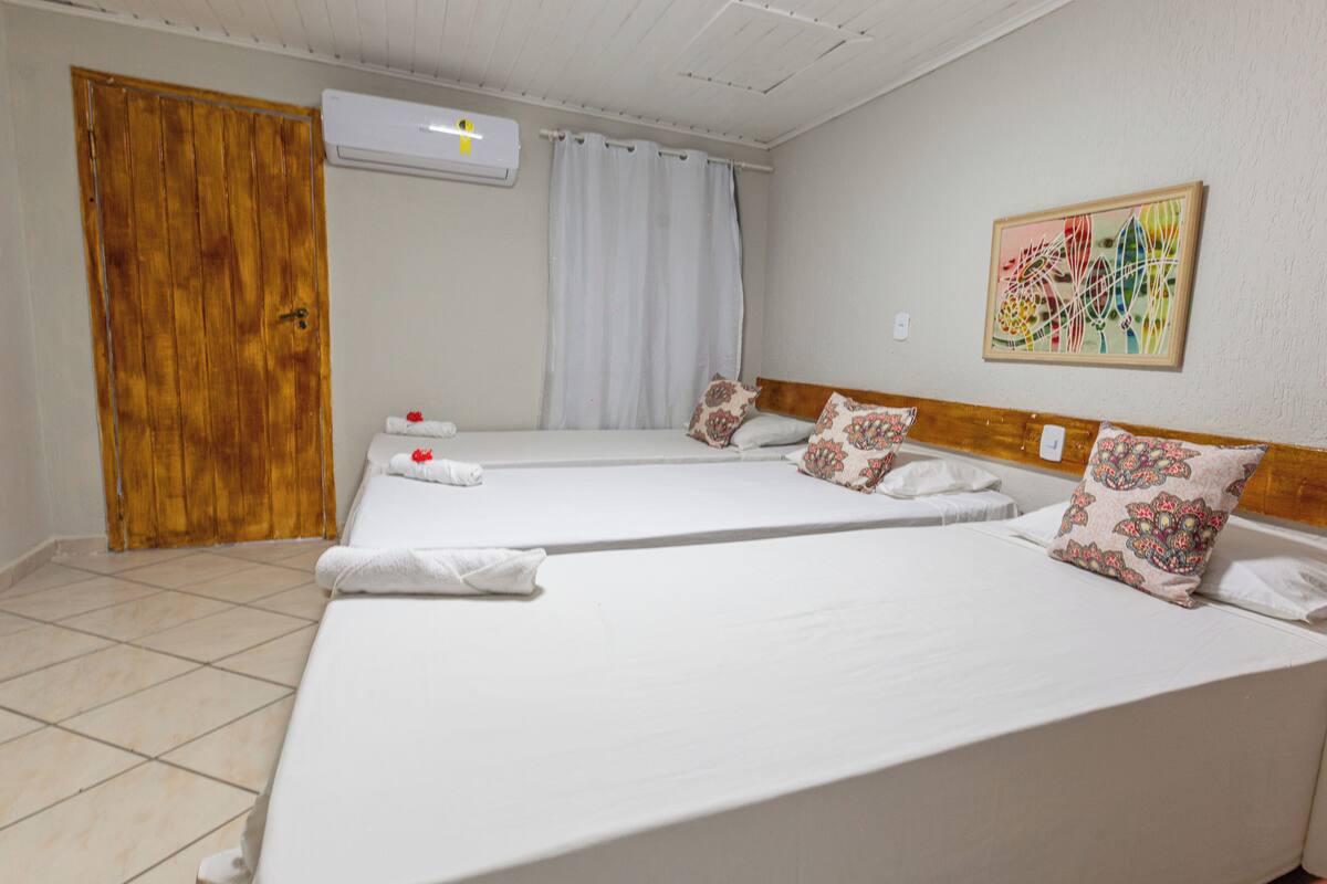 A hotel room with two beds, a wooden door, an air conditioning unit, and a colorful painting on the wall.