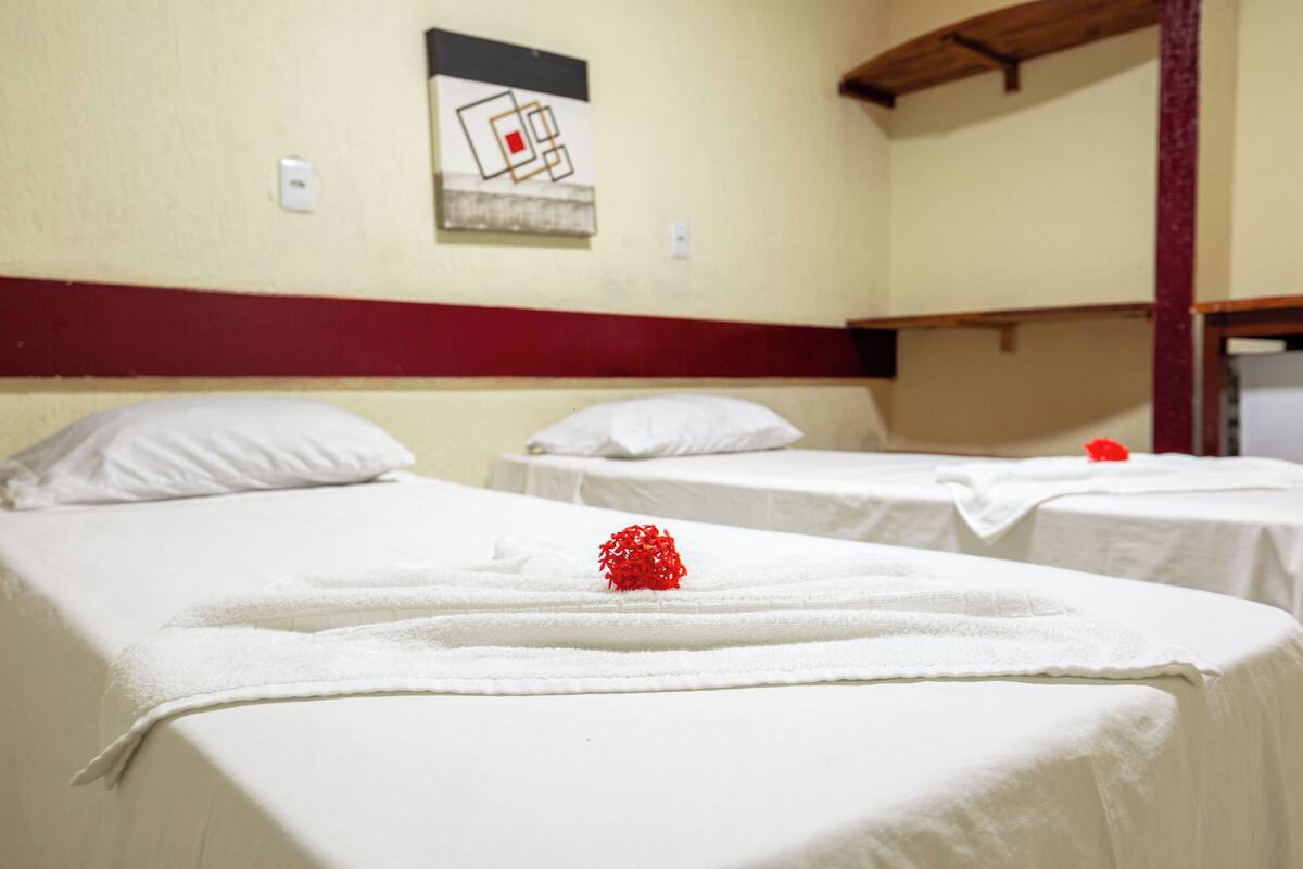 A hotel room with two beds, each with a white bedspread and pillows, and a red decorative item on the bed.