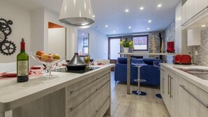 A modern kitchen with a central island, a dining area with a blue sofa, and a red toaster.