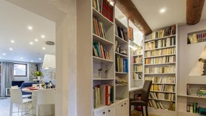 A modern living room with a dining area, a large bookshelf filled with books, and a wooden ceiling beam.