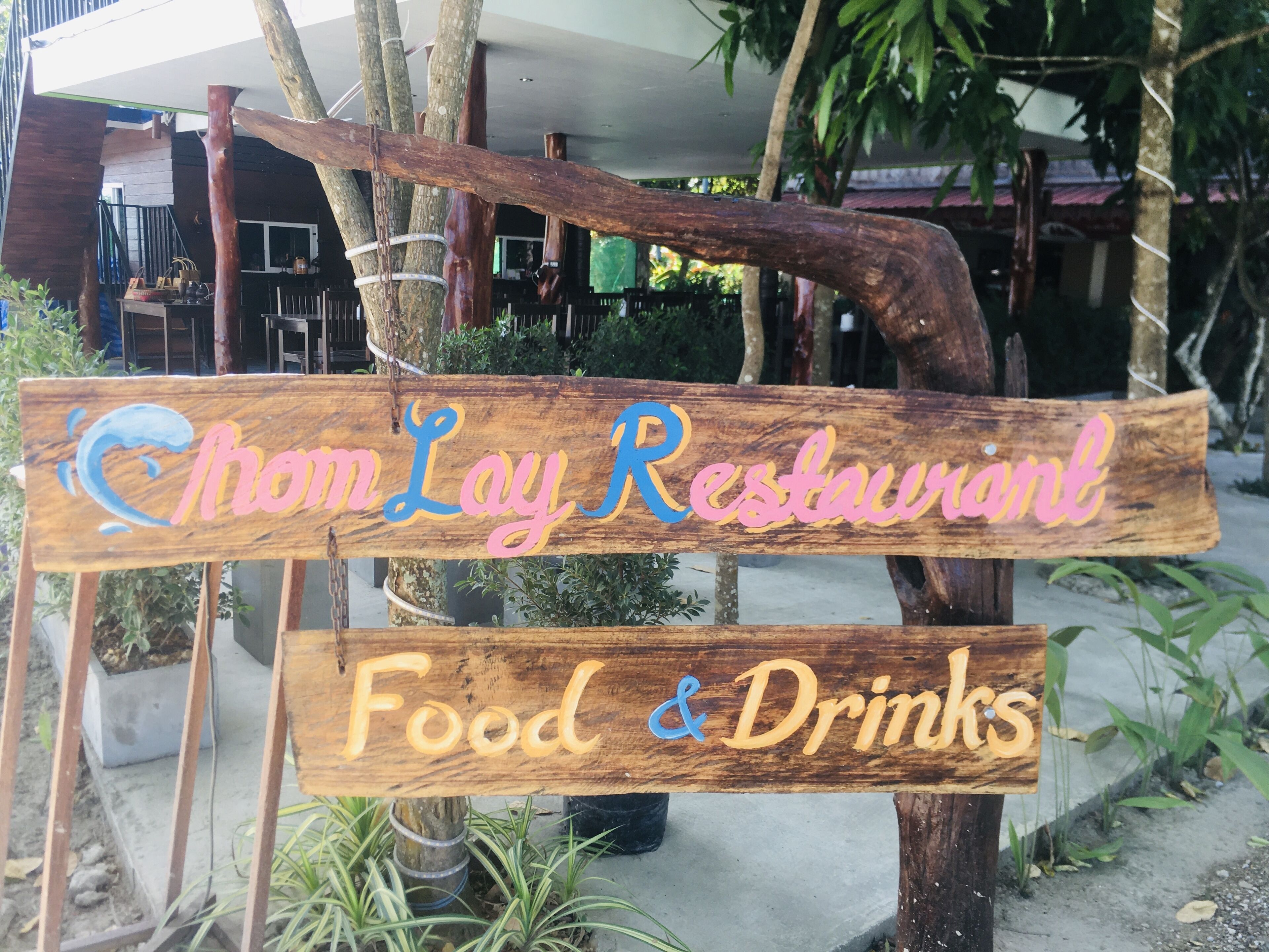 A wooden sign for 'Chom Lay Restaurant' with 'Food & Drinks' written below.
