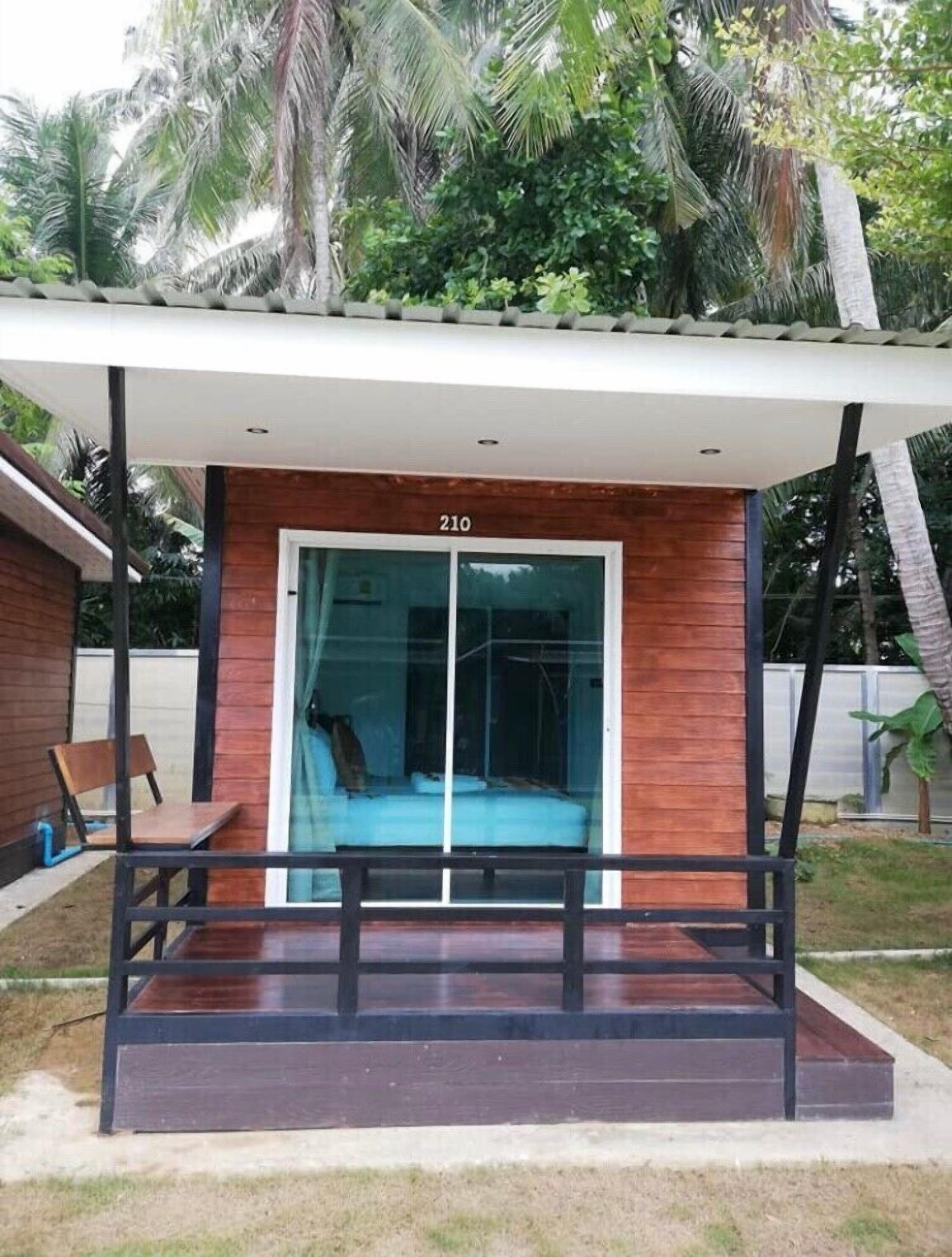 A modern building with a wooden facade and a glass door, numbered 210, with a bench and a small table in front.