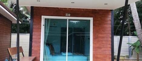 A modern building with a wooden facade and a glass door, numbered 210, with a bench and a small table in front.