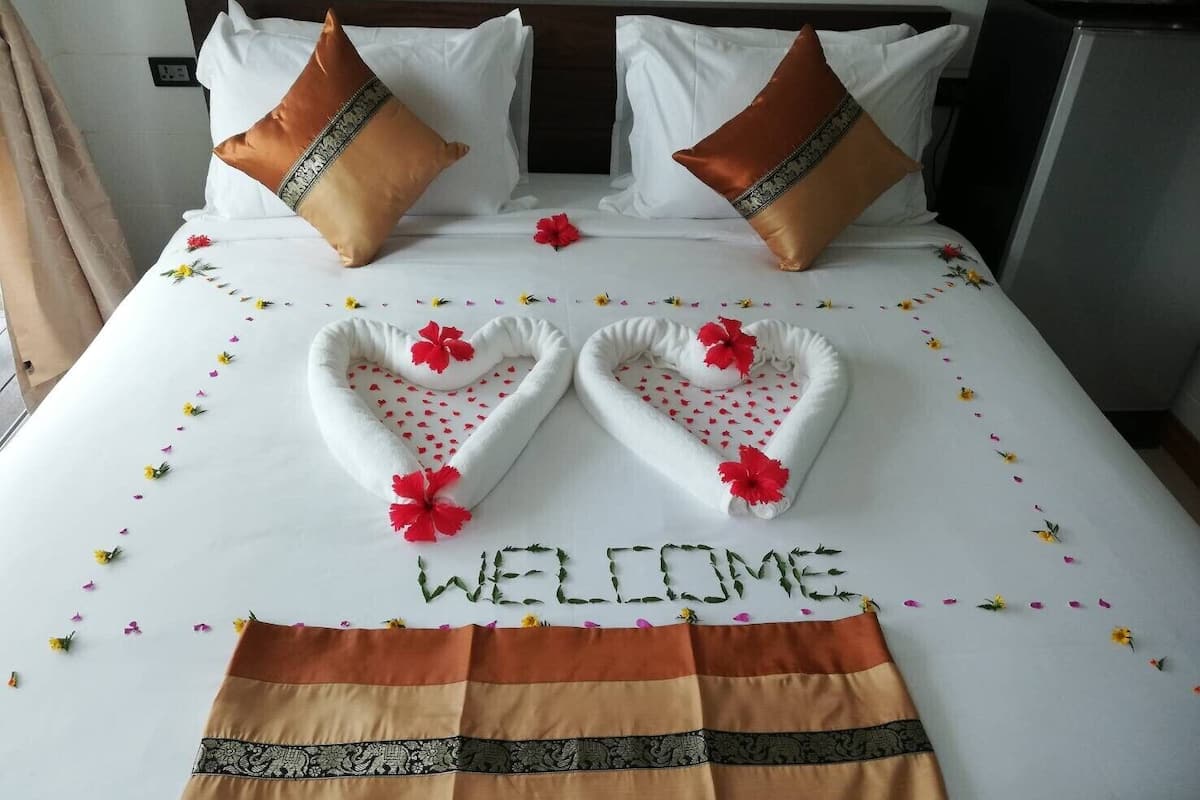 A bed with white linens, two brown pillows, heart-shaped floral arrangements, and a welcome mat.