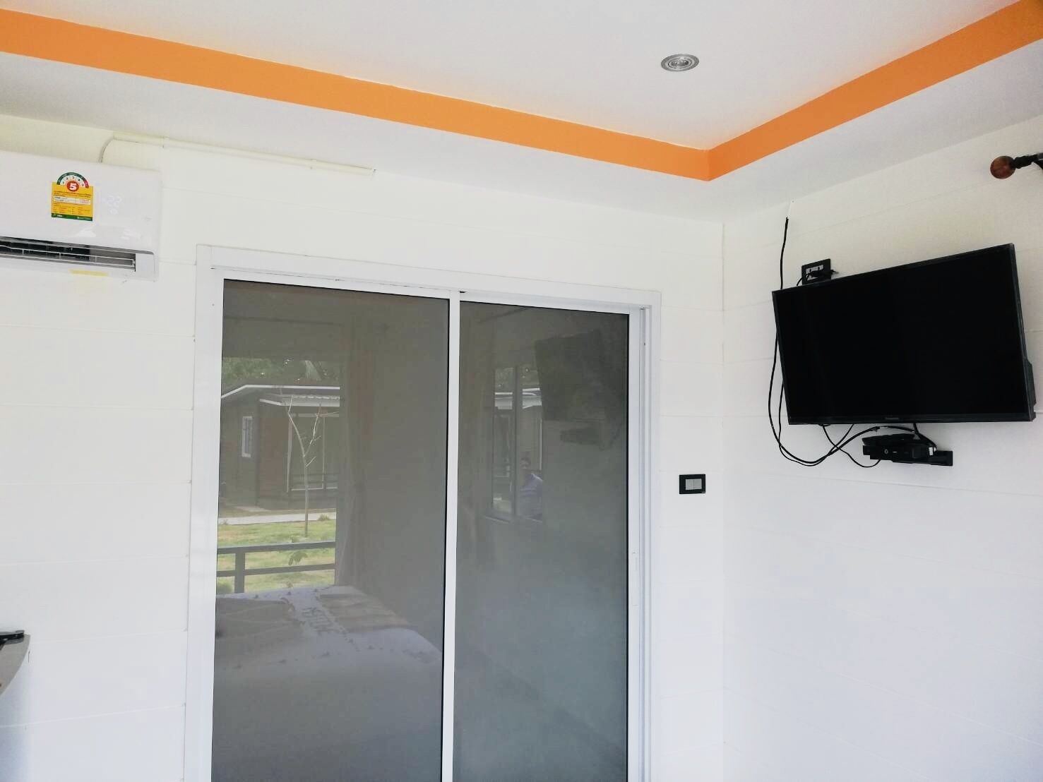 Una habitación con puerta de vidrio corrediza, televisión montada y unidad de aire acondicionado.