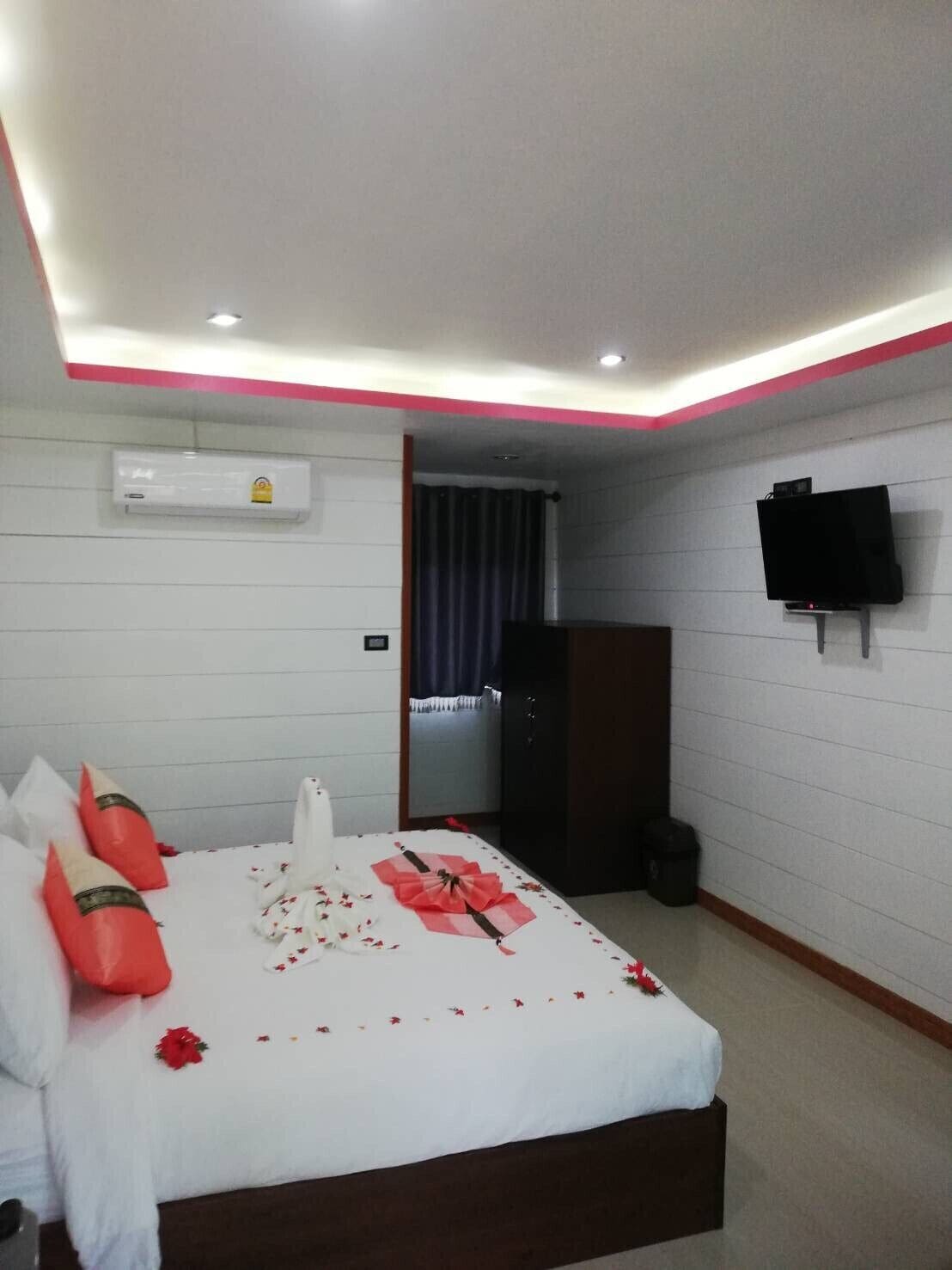 A hotel room with a neatly made bed, a television mounted on the wall, and an air conditioning unit.
