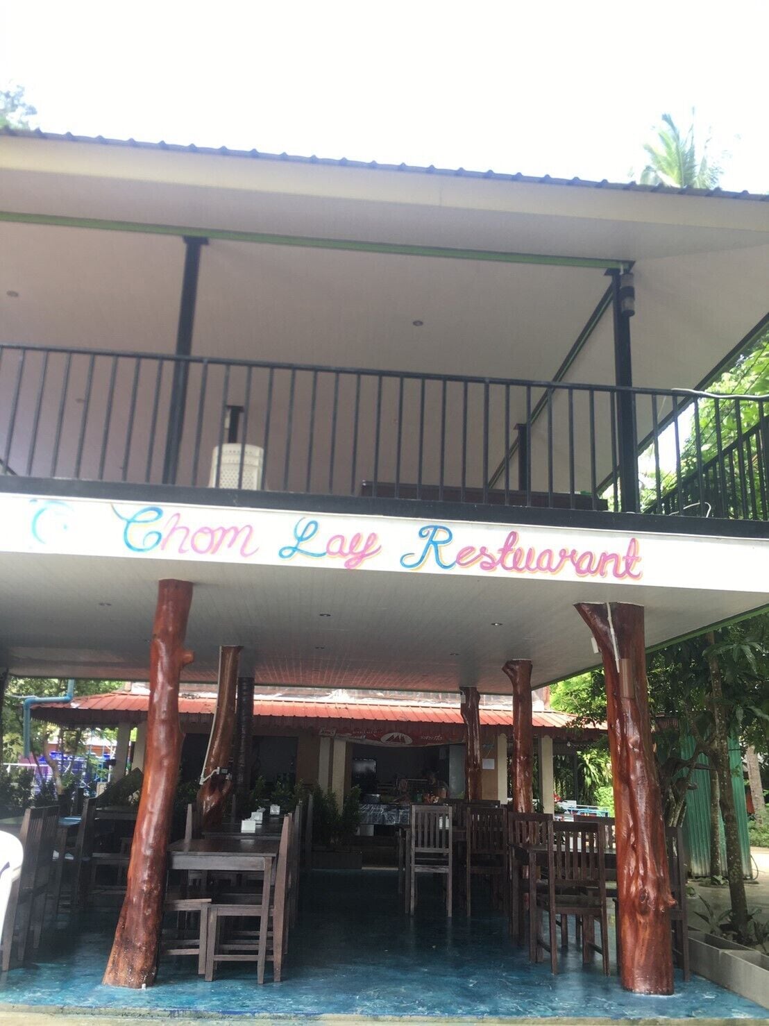 Un restaurante con un letrero que dice "Chom Lay Restaurant" sostenido por estructuras que parecen árboles.