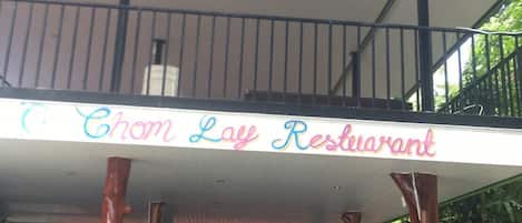 Un restaurante con un letrero que dice "Chom Lay Restaurant" sostenido por estructuras que parecen árboles.