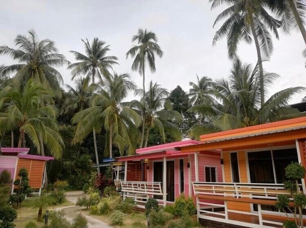 A row of colorful cabins with a tropical backdrop, surrounded by lush greenery and palm trees. - Phumiphat Resort Koh Mook (Ko Mook)