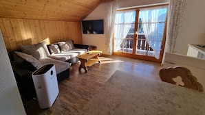 Una sala de estar acogedora con techo de madera, un sofá, una mesa de centro y un ventanal corredero que da a un balcón.