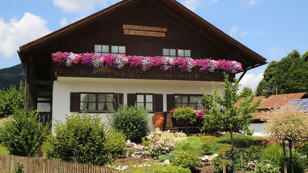 Un edificio tradicional de madera con un balcón decorado con flores, rodeado por un jardín cuidado.