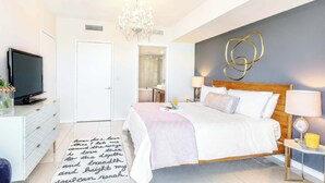 Ein modernes Schlafzimmer mit einem großen Bett, einem Fernseher, einer Kristallleuchtre und einem Wandkunstwerk.