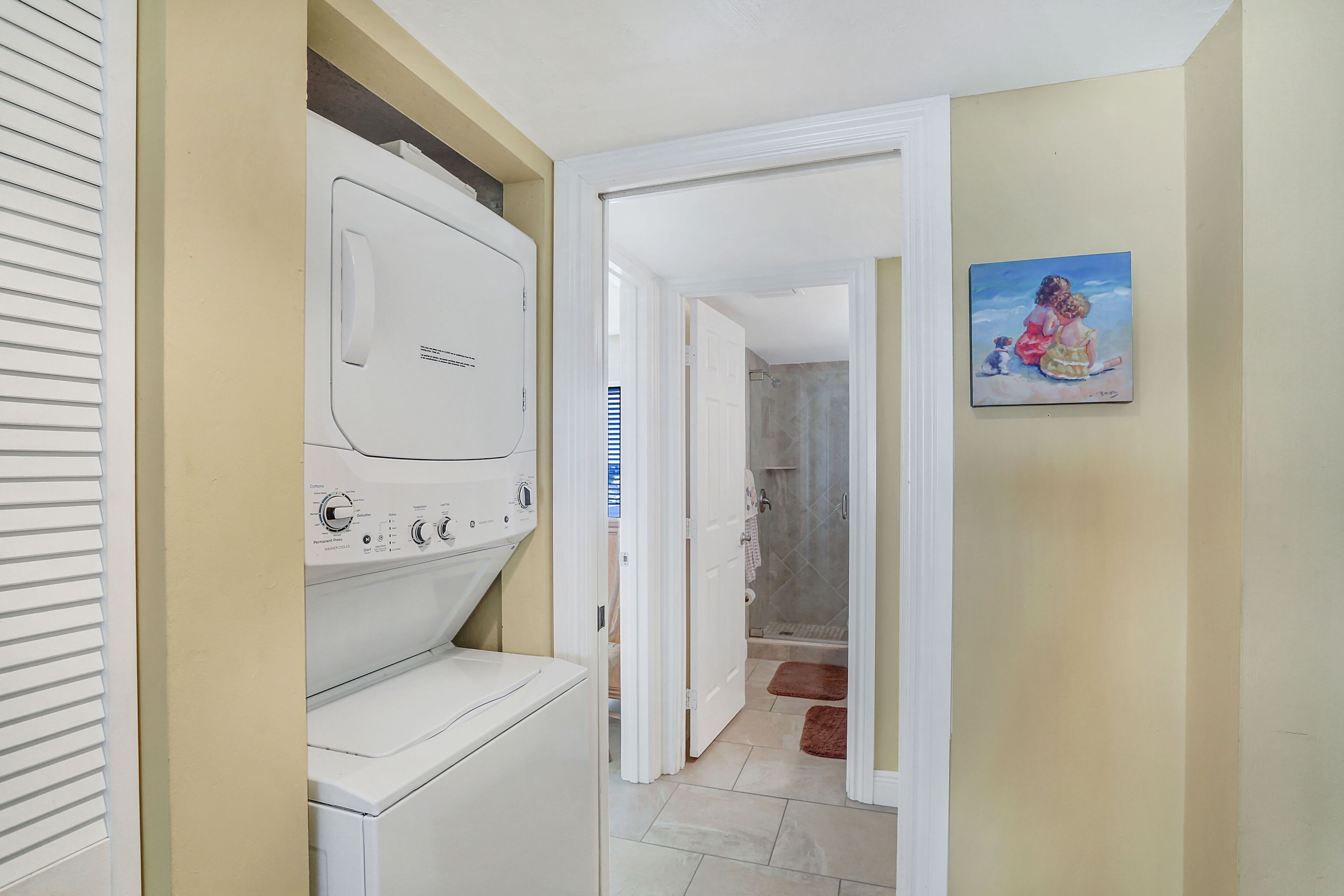 Een wasserette met een voorlader wasmachine en droger, een gang naar een badkamer, en een schilderij aan de muur.