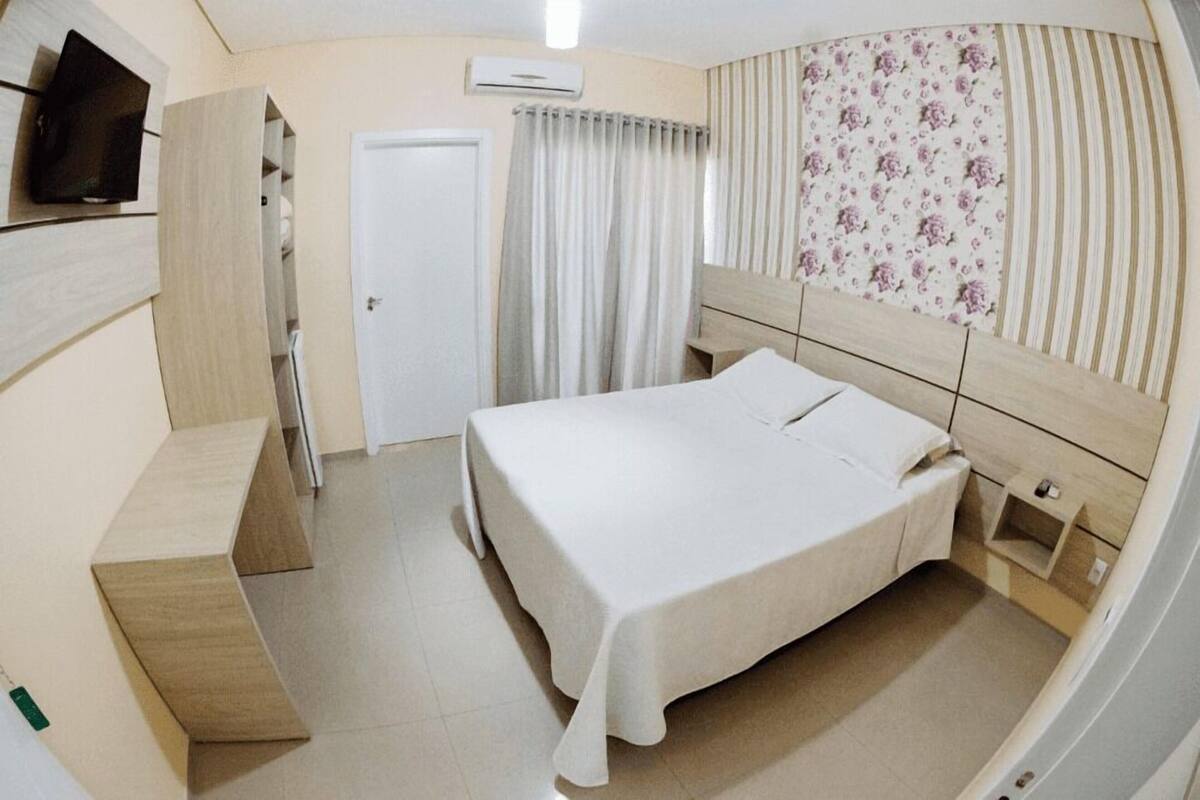 A bedroom with a bed, a TV, a wardrobe, a door, and a curtain.