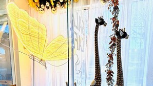 A reception area with a glass door, a yellow decorative umbrella, two giraffe statues, and a basket of yellow flowers. - Hotel Natal (Penha)